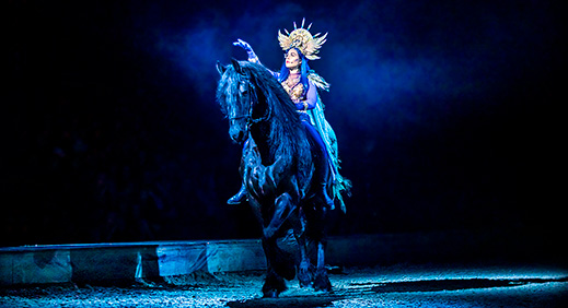 Woman on stage with a black Friesian 