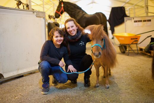 Kind und Frau hocken neben Mini Shetlandpony