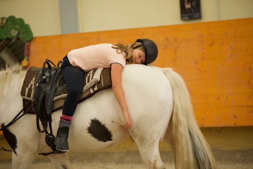 Tyttö makaa vatsallaan hevosen selkää vasten